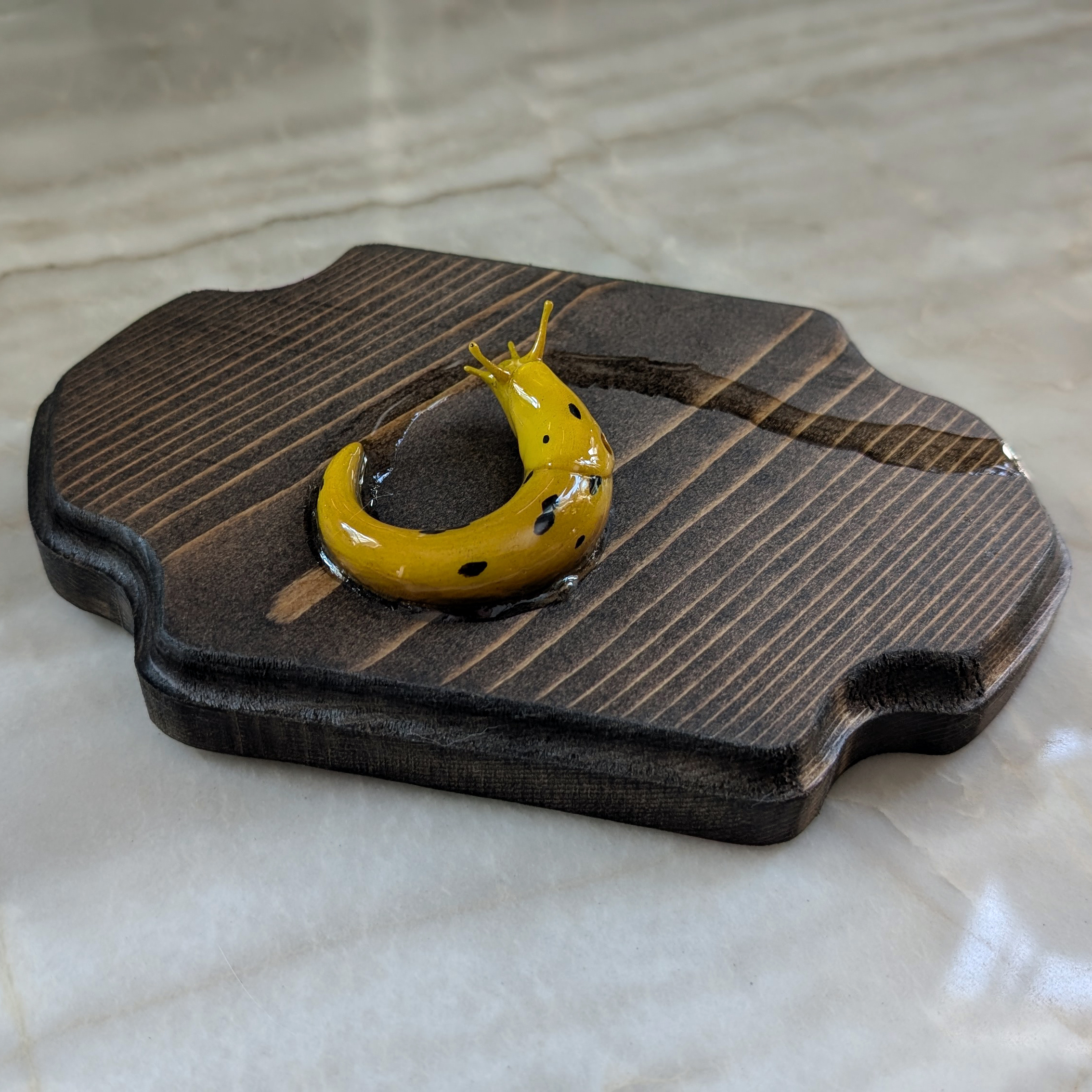 A yellow slug with black spots resting on a wooden base with a smooth surface.