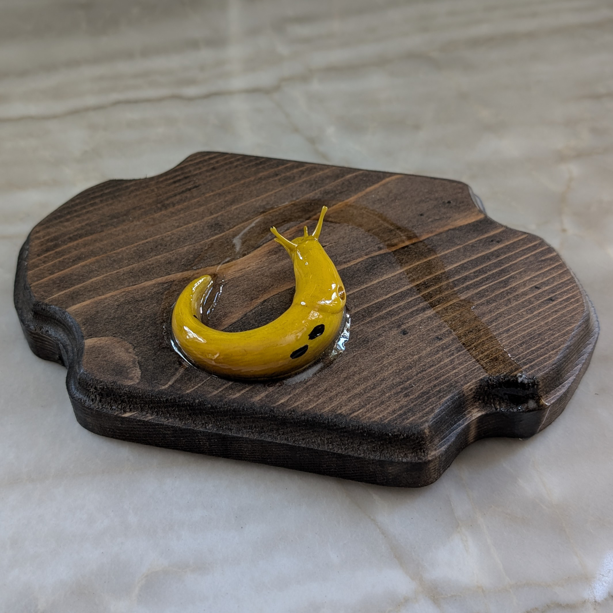 A yellow slug resting on a dark wooden board with a smooth surface.